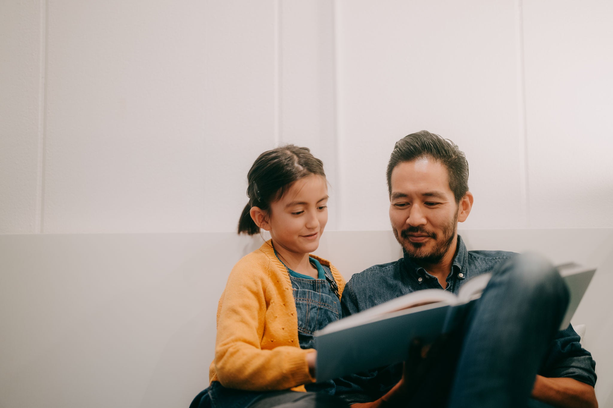 Father and young daughter reading book together at home