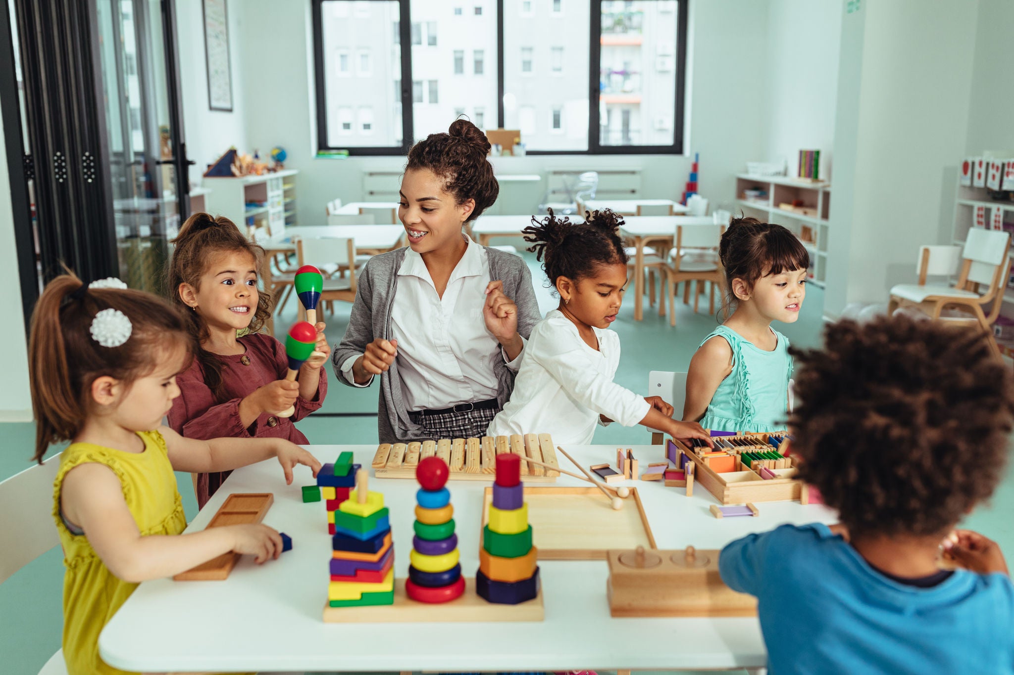 Kids and teacher sitting at the table and playing with toys