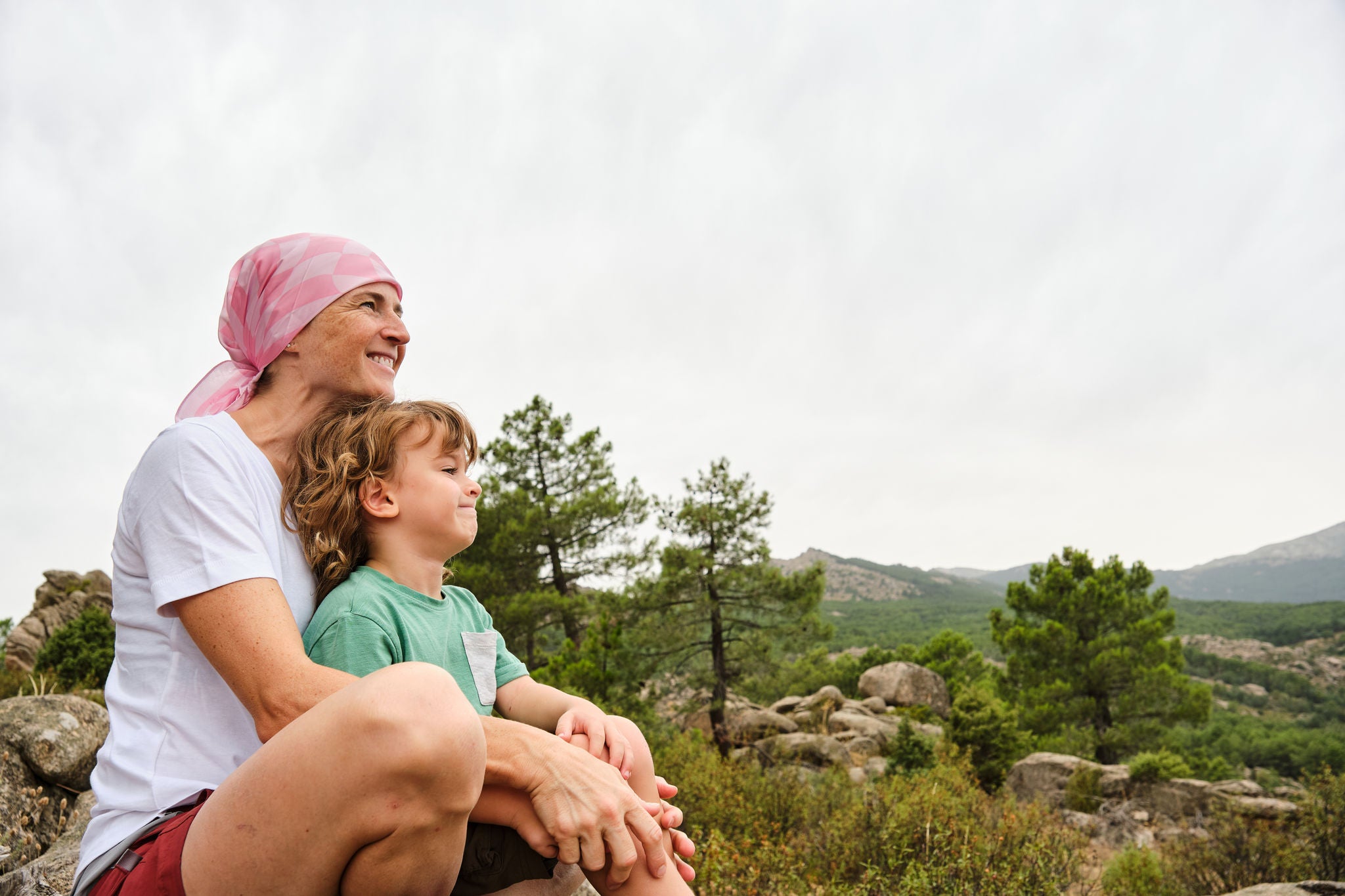 Woman with cancer enjoying nature with her son. She is wearing a pink headscarf.