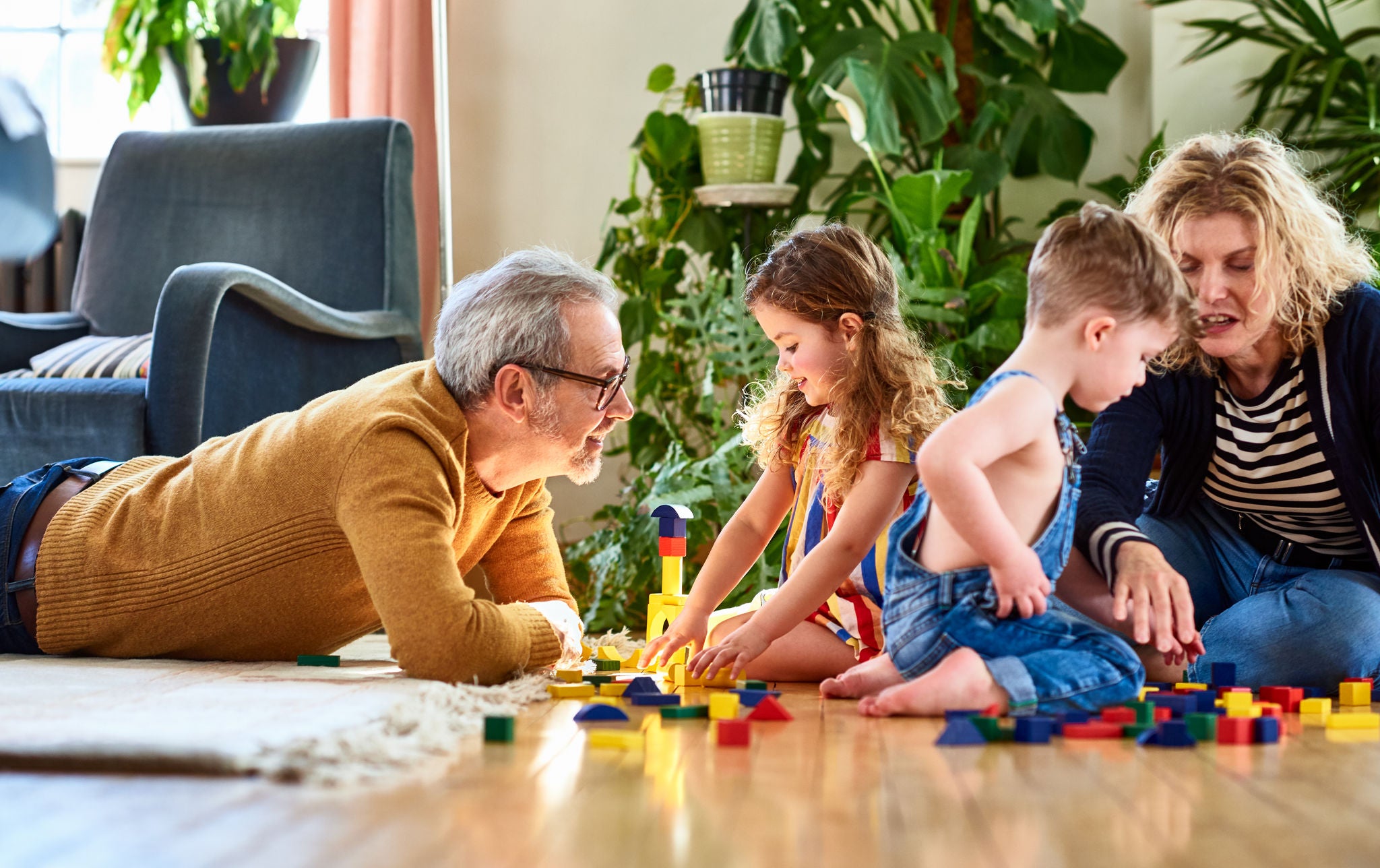 Active grandparents looking after their two grandchildren at home, playing with wooden toy blocks, having fun, learning, development, togetherness
