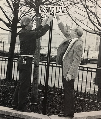 Edmund Genier (right), then vice president for real estate, with assistance of Terry Meinders place Kissing Lane sign outside the tower.